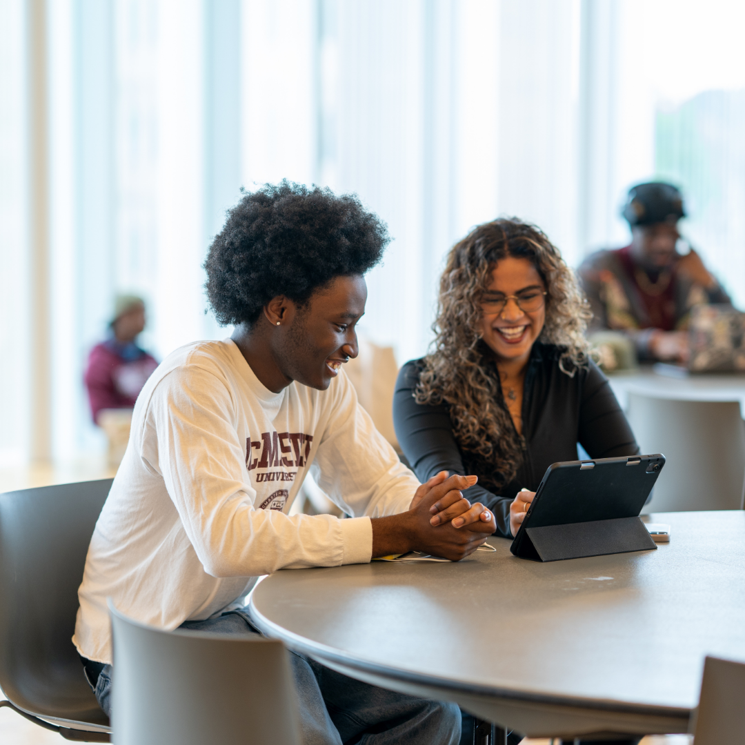 A staff member and student smiling as they look at a tablet.